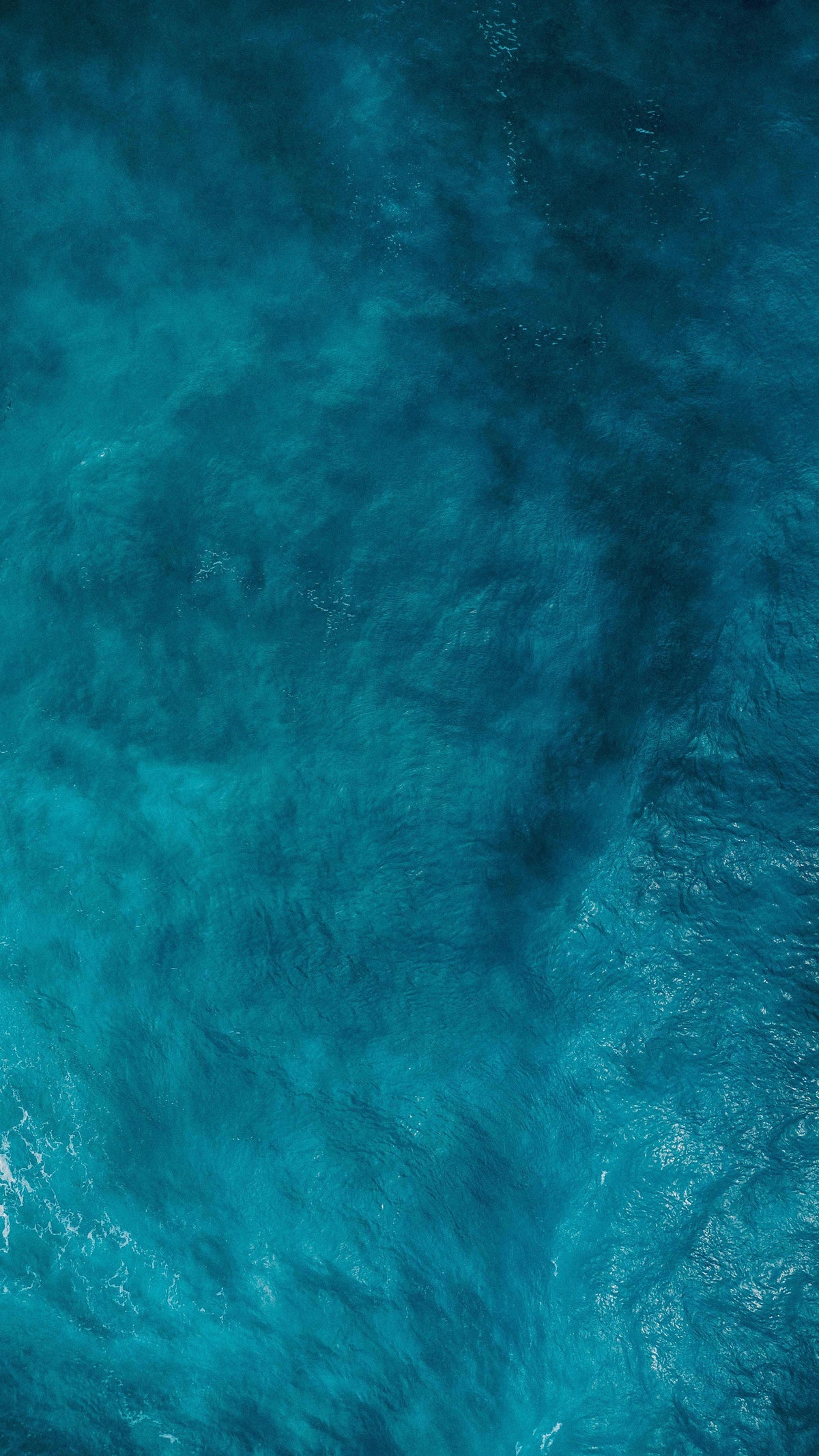 Aerial view of deep blue ocean water with subtle waves and light reflection.